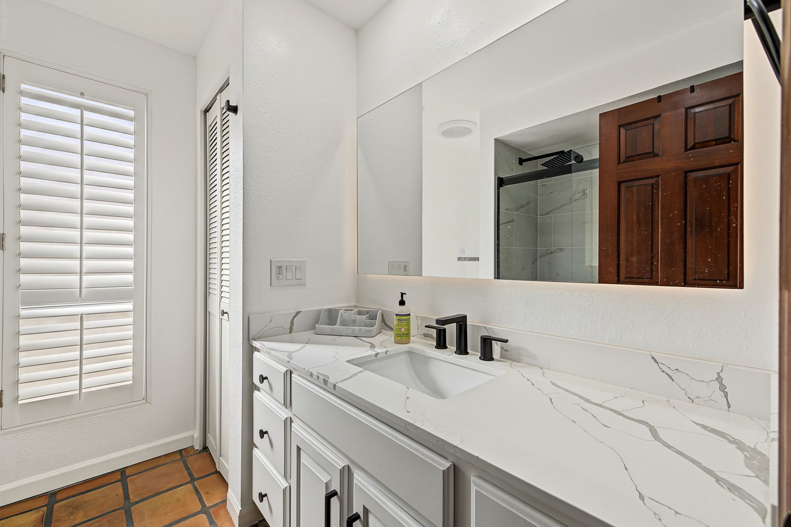 Updated bathroom with a quartz vanity, black fixtures and plantation shutters